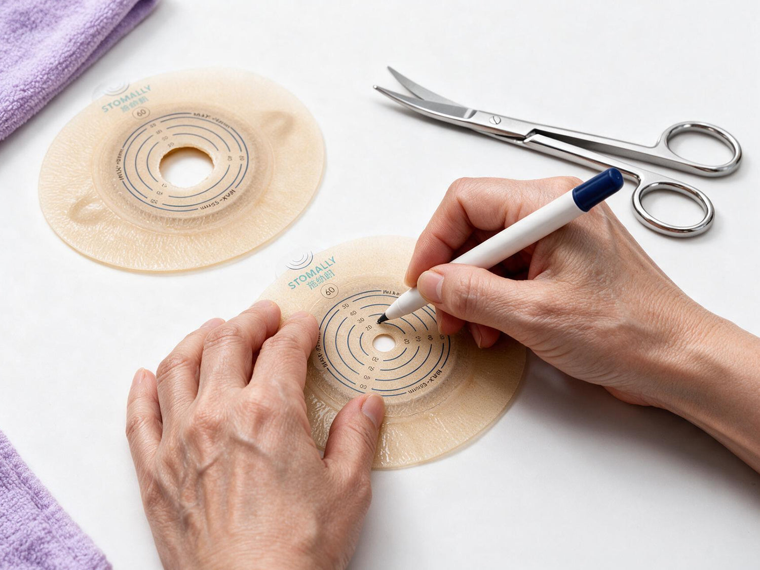 Hands measuring and marking an ostomy skin barrier on a clean surface